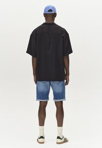 Črna oversize srajca, kratke jeans hlače s preklopom, modra kapa, bele nogavice in črne teniske z belimi ter svetlo rjavimi poudarki.