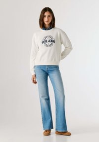 Λευκό φούτερ με λογότυπο "PEPE JEANS" σε σκούρο μπλε χρώμα, συνδυασμένο με ανοιχτό μπλε τζιν παντελόνι με φλέρτ. Το σύνολο χαρακτηρίζεται από απλό, καθημερινό σχέδιο και απαλά υφάσματα.