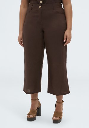 Pantalon court marron taille haute avec boutons sur le devant, porté avec des talons compensés beige, présenté sur une personne debout sur un fond uni.