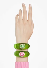 Gröna akrylnitar, en med en grön ädelsten och en med en rosa ädelsten, båda med oktagonala former och klara stenar som dekoration.