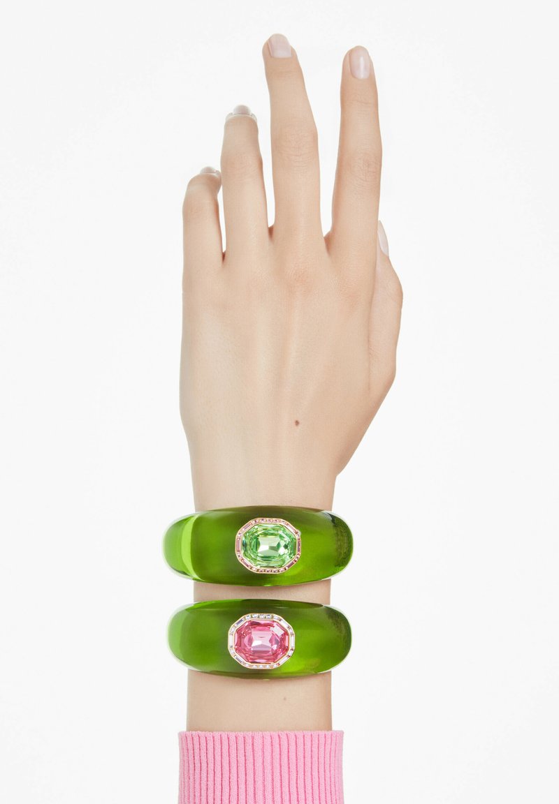 Gröna akrylnitar, en med en grön ädelsten och en med en rosa ädelsten, båda med oktagonala former och klara stenar som dekoration.