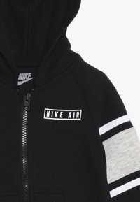 Zwarte rits hoodie met een kangoeroezak, voorzien van het "Nike Air" logo, grijs-witte gestreepte manchetten en een textuurstof.