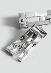 Spilla d'argento con cristalli chiari rettangolari e geometrici di varie dimensioni. Il design include un meccanismo di chiusura circolare.