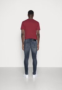 Camiseta marrón y jeans azul oscuro combinados con zapatillas blancas. Enfocarse en el diseño ajustado y la textura suave de la ropa.