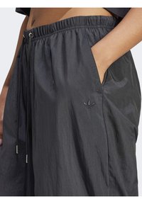 Mustat kevyet shortsit, joissa on joustava vyötärö, nyöritys, sivutaskut ja brodeerattu logo. Silky, teksturoitu pinta.