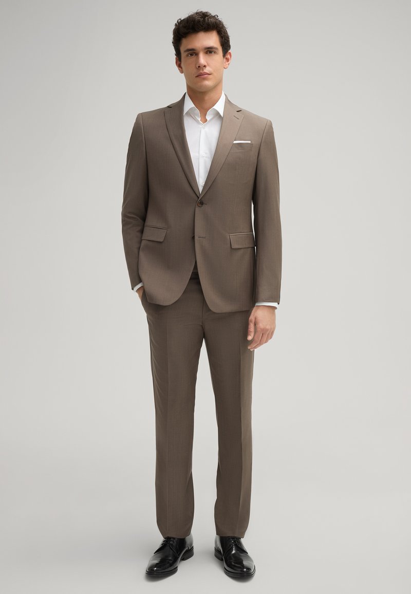 Brauner Maßanzug mit einem Zwei-Knopf-Jacket, Reverskragen und seitlichen Taschen; kombiniert mit einem weißen Hemd und schwarzen Lederschuhen.
