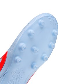 Világoskék focicipő talp piros részletekkel, melynek bőrét tüskés tapadási pontok és texturált felület jellemzi, a jobb tapadás és irányítás érdekében.