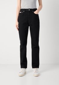 Jeans di denim neri con taglio dritto, design a cinque tasche e chiusura con bottone. Tessuto testurizzato con una sottile lucentezza. Sneakers bianche completano l'outfit.