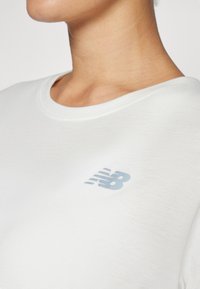 Balta trumpa rankovė T-shirt, pagaminta iš minkštos medžiagos, su šviesiai mėlynu logotipu kairėje krūtinės pusėje. Apvalus iškirpimas, paprastas dizainas.
