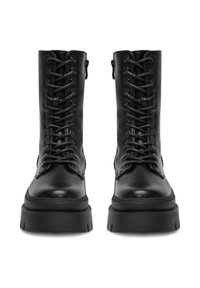 Para czarnych skórzanych butów wojskowych zapinanych na sznurowadła z grubymi, masywnymi podeszwami, widok z przodu na białym tle.