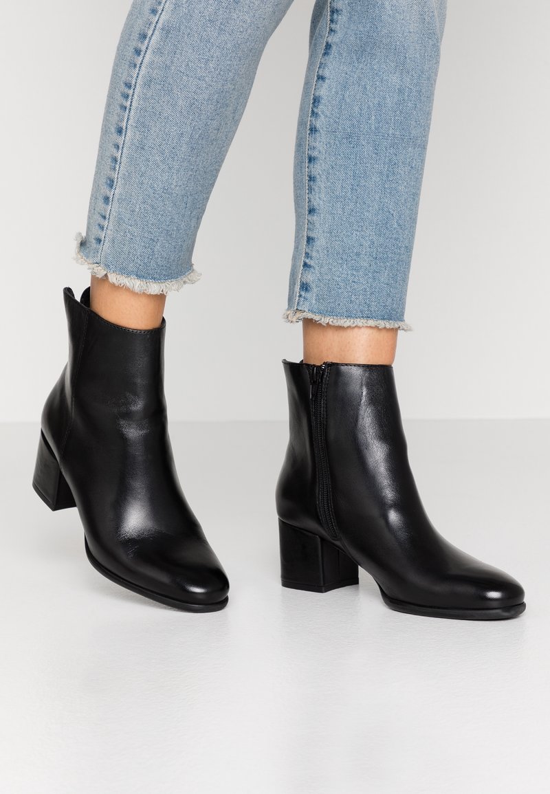 Bottes cheville en cuir noir avec bout pointu et talon bloc. Fermeture éclair latérale, texture lisse, et design élégant. Revers en denim délavé.