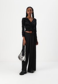 Μαύρη βελούδινη μπλούζα με σχέδιο σε σχήμα διαμαντιού, σε συνδυασμό με μαύρο παντελόνι με ψηλή μέση και φαρδιά πόδια και μια ασημένια μεταλλική τσάντα.