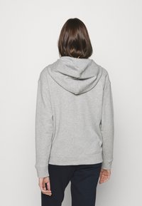 Sweatshirt à capuche gris en tissu doux, avec une coupe décontractée, des poignets et un ourlet en côte. La capuche est en trois parties avec une couture.