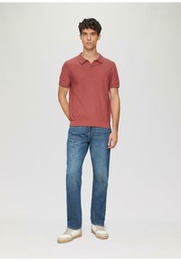 Kurzärmliges Poloshirt in einem staubigen Rosaton, kombiniert mit blauen Denim-Jeans und weißen Sneakern mit beigefarbenen Akzenten. Flache Textur.