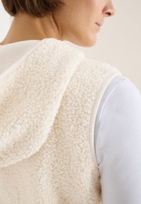 Cremefarbige Fleeceweste aus strukturiertem, geschlungenem Material; mit Kapuze und kontrastierendem, glattem Stoff an den Rändern.