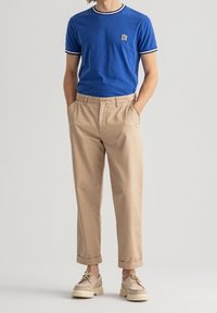 Niebieska bawełniana koszulka z białym paskowanym kołnierzem i mankietami, zestawiona z beżowymi chinosami, o gładkiej fakturze i podwiniętych nogawkach.