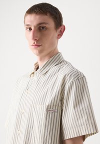 Short-sleeve, cream-striped shirt with blue lines, featuring a button-up front and a small Calvin Klein label on the chest pocket.