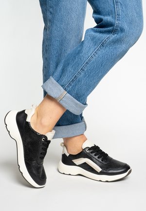 Schwarze Turnschuhe mit strukturiertem Mesh und glatten Lederakzenten, ausgestattet mit weißer Sohle und Schnürsenkeln, getragen zu hochgekrempelten blauen Jeans.