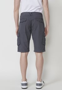 Grijze cargoshorts met meerdere zijzakken, een relaxte pasvorm, gestructureerde stof en een trekkoord in de taille, gedragen met witte sneakers.