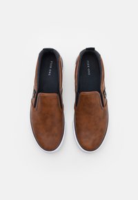 Chaussures à enfiler marron en simili cuir avec une finition lisse, semelle en caoutchouc blanche et accents élastiques pour un enfilage facile.