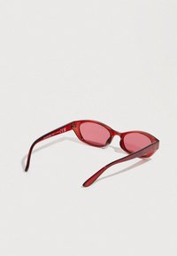 Lunettes de soleil rouges avec une monture ovale fine, dotées de verres rouges translucides. Les branches sont lisses et légèrement courbées.