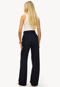 Pantalon large bleu marine avec une taille haute, un tissu texturé, et deux poches arrière, porté avec un débardeur blanc.