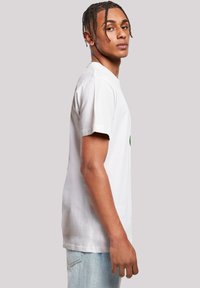 White cotton t-shirt with short sleeves, round neckline, and a green graphic on the chest, paired with light blue denim jeans.