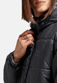 Zwarte gewatteerde jas met capuchon, voorzien van een doorgestikt ontwerp, elastische manchetten en een subtiel merklogo op het borstgedeelte.