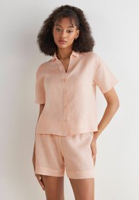 Pfirsichfarbendes Leinenhemd mit kurzen Ärmeln und Knopfleiste, kombiniert mit passenden Shorts. Der Stoff ist texturiert und leicht und bietet eine lockere Passform.