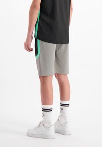 Grijze sportshorts met zwarte en groene accenten, gecombineerd met witte sneakers en geribde sokken met een gestreept patroon.