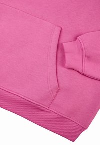 Rozā sporta krekls ar ribotu apakšmalu un piedurknēm, ar kangaro kabatu un gludu tekstūru. Tuvplāns uzsver šuvju detaļas.