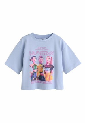 Hellblaues Baumwoll-Bauchfreies Top mit einem lebendigen Grafikdruck von drei Charakteren mit verschiedenen Frisuren und Outfits, beschriftet mit "ZOEY, RUMI, MIRA".