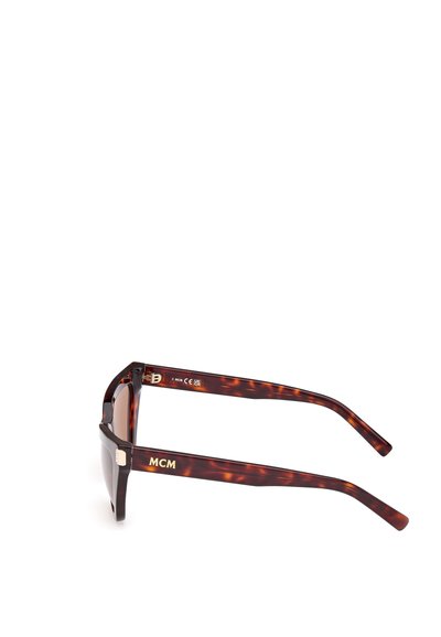 Ochelari de soare cu rame tortoise, cu lentile rectangulare, rame groase și branding „MCM” aurii pe tâmple. Textură netedă, design modern.