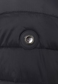 Tissu d'un manteau en duvet noir avec une texture lisse, présentant un bouton métallique rond proéminent et des détails de couture subtils.