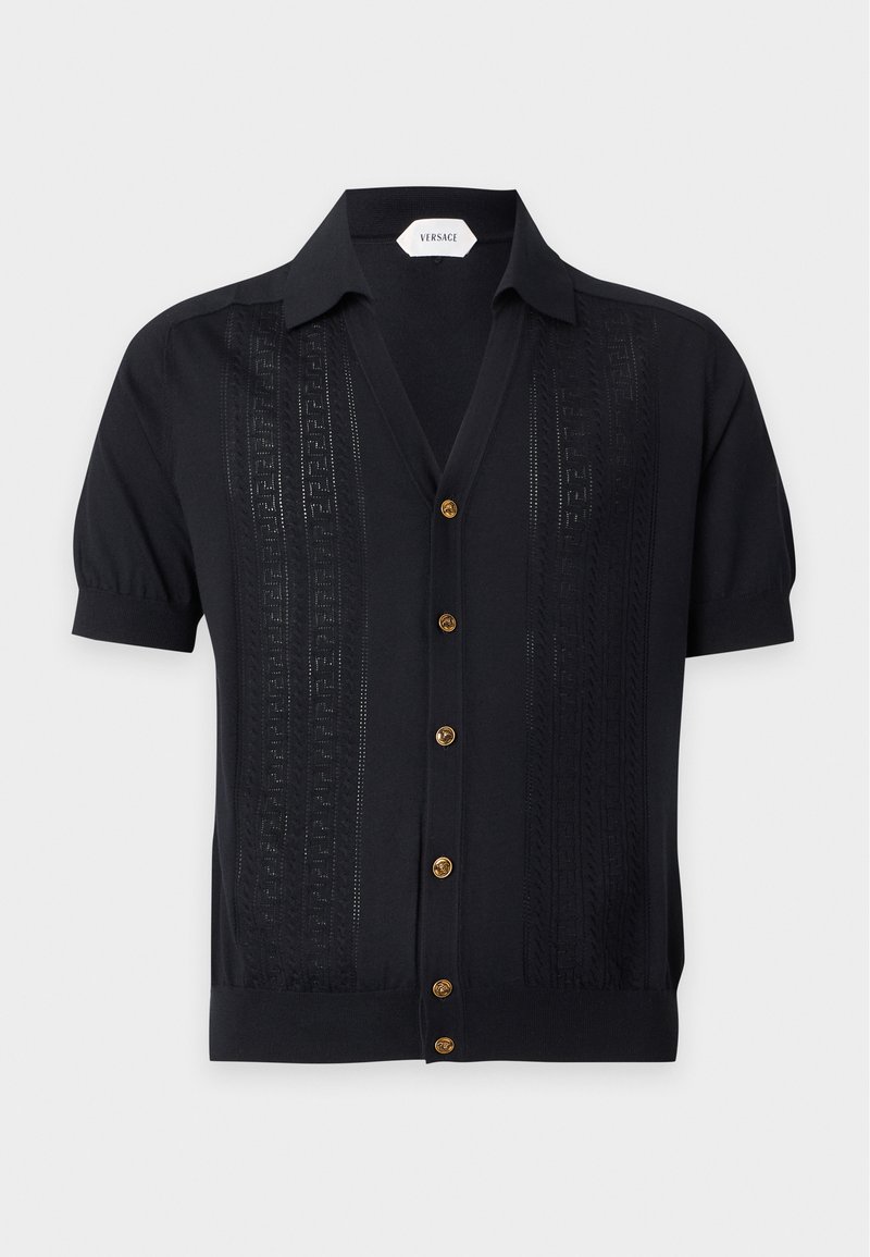 Chemise noire à manches courtes avec boutons dorés, motifs verticaux texturés subtils, et un col, étiquetée Versace à l'intérieur du col.