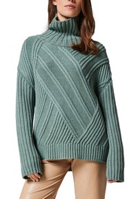 Miętowo-zielony sweter robiony na drutach z wysokim kołnierzem, z teksturowanymi przekątnymi i pionowymi wzorami oraz oversize'owymi rękawami.