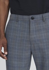 Šedé kárované kalhoty s knoflíkovým zapínáním a páskem v pase. Tkanina má texturovaný vzhled s modrými a hnědými proužky v kostkovaném vzoru.