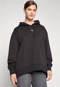 Felpa nera con cappuccio realizzata in tessuto misto cotone, dotata di tasca frontale, cappuccio con cordino e patch con logo sul petto. Design a vestibilità rilassata.