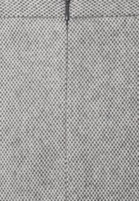 Gros plan d’un tissu texturé à carreaux gris et blanc avec une fermeture éclair noire centrée, partiellement visible en haut.