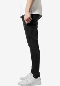 Černé úzké džíny s hladkou texturou, s klasickým designem pěti kapes, nošené s bílými sportovními teniskami.