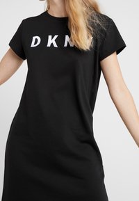 Černé krátké tričko šaty z bavlny, s bílým logem "DKNY" na hrudi, volný střih a délka ke kolenům.