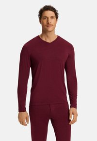 Burgundská dlouhá vesta s výstřihem do V vyrobená z měkké tkaniny, úzký střih s plochými švy, doplněna slim-fit kalhotami ve stejném odstínu.