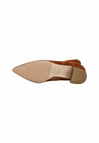 Scarpa in suede marrone con punta affusolata e suola beige liscia. Presenta una forma snella ed elegante con una texture sottile e un design minimalista.