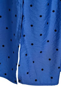 Blauer Stoff mit verstreuten schwarzen Punkten, der eine Naht und leichte Falten zeigt.