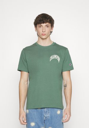 T-shirt in cotone verde con colletto girocollo, caratterizzato dal logo bianco "CHAMPION" sul lato sinistro del petto e un piccolo logo sul lato destro della manica. Maniche corte.