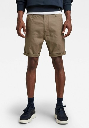 Shorts en coton kaki avec des ourlets retroussés, dotés de poches avant diagonales et d'une fermeture éclair, associés à des baskets et chaussettes bleu marine.