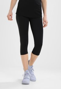 Leggings capri noirs en tissu lisse et extensible, avec une coupe ajustée se terminant au milieu du mollet, associés à des chaussures de sport bleu clair.