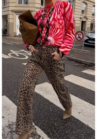 Suéter de punto colorido con patrones florales llamativos en rojo y rosa, combinado con pantalones de estampado de leopardo. El conjunto incluye un bolso marrón y botas beige.