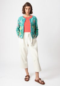 Cárdigan turquesa con patrones florales, top de color coral y culottes color crema. Sandalias marrones con correas y acentos. Diseño de corte relajado.