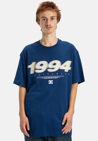 Marinblå oversized t-shirt i bomull, med året "1994" i stor vit text och en liten logotyp i mitten längst ner.